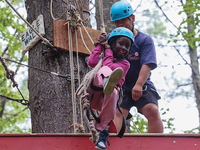 Camper at Double H Ranch participates in ropes course with the support of a camp staffer