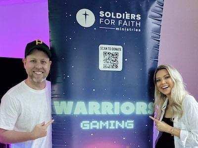 Adults pose next to a Warriors Gaming sign that promotes healthy communities using video games