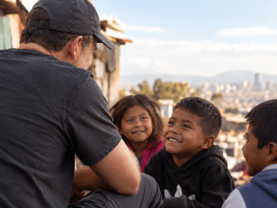 Volunteer speaking with smiling children during a community outreach visit, representing Hope of the Poor’s mission.